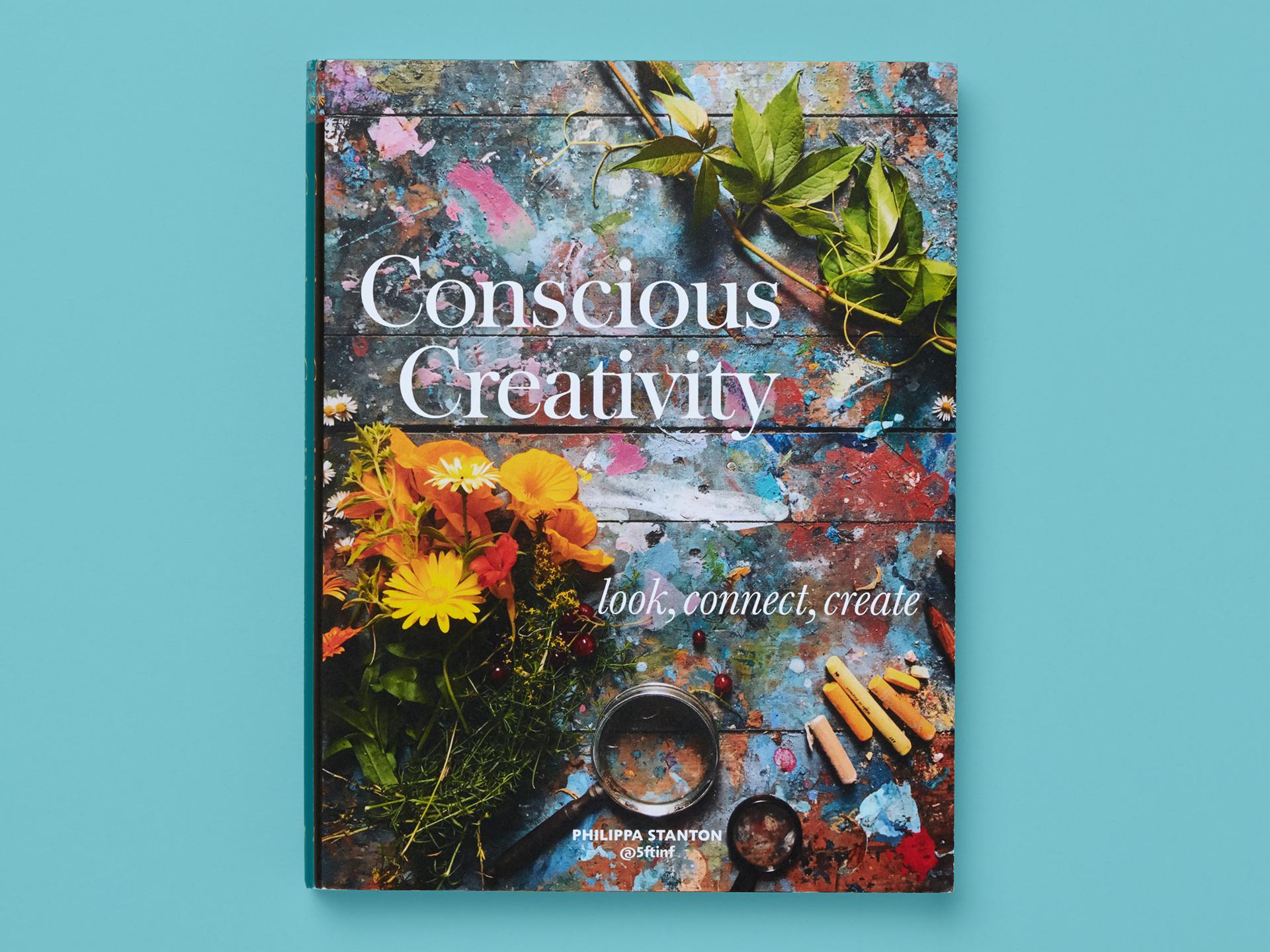 Book entitled "Conscious Creativity" on a teal background. Cover shows a paint-splattered wooden surface with flowers, leaves, chalk sticks, and a magnifying glass arranged across it. White title text reads "Conscious Creativity" with the subtitle "look, connect, create," and author Philippa Stanton is credited at the bottom.