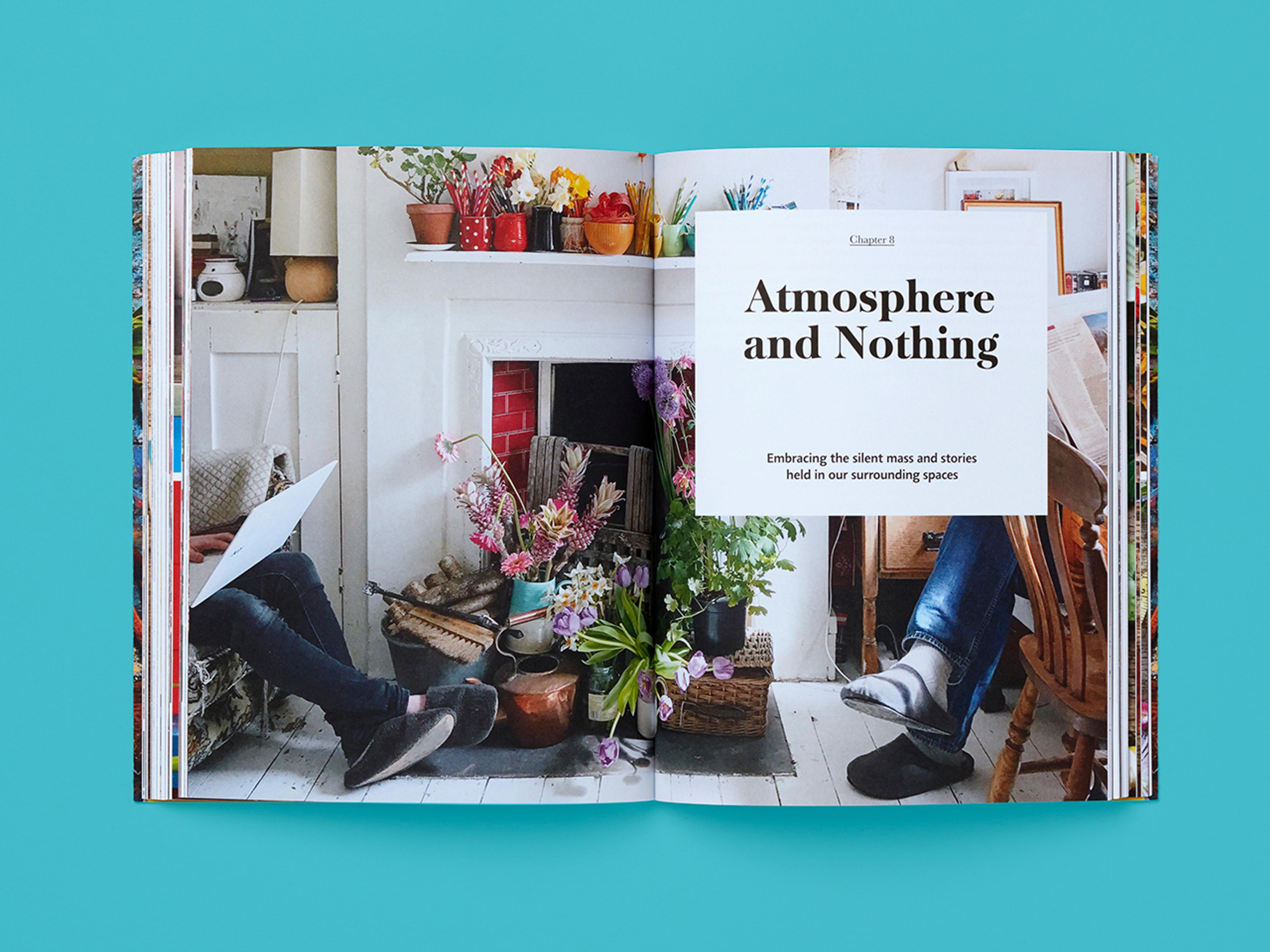 Open book spread from Conscious Creativity showing a chapter opener titled “Atmosphere and Nothing,” with the subtitle “Embracing the silent mass and stories held in our surrounding spaces.” A full-bleed photograph depicts a lived-in studio interior with a fireplace, flowers in vases, art tools on shelves, and two seated figures partially visible at either side.