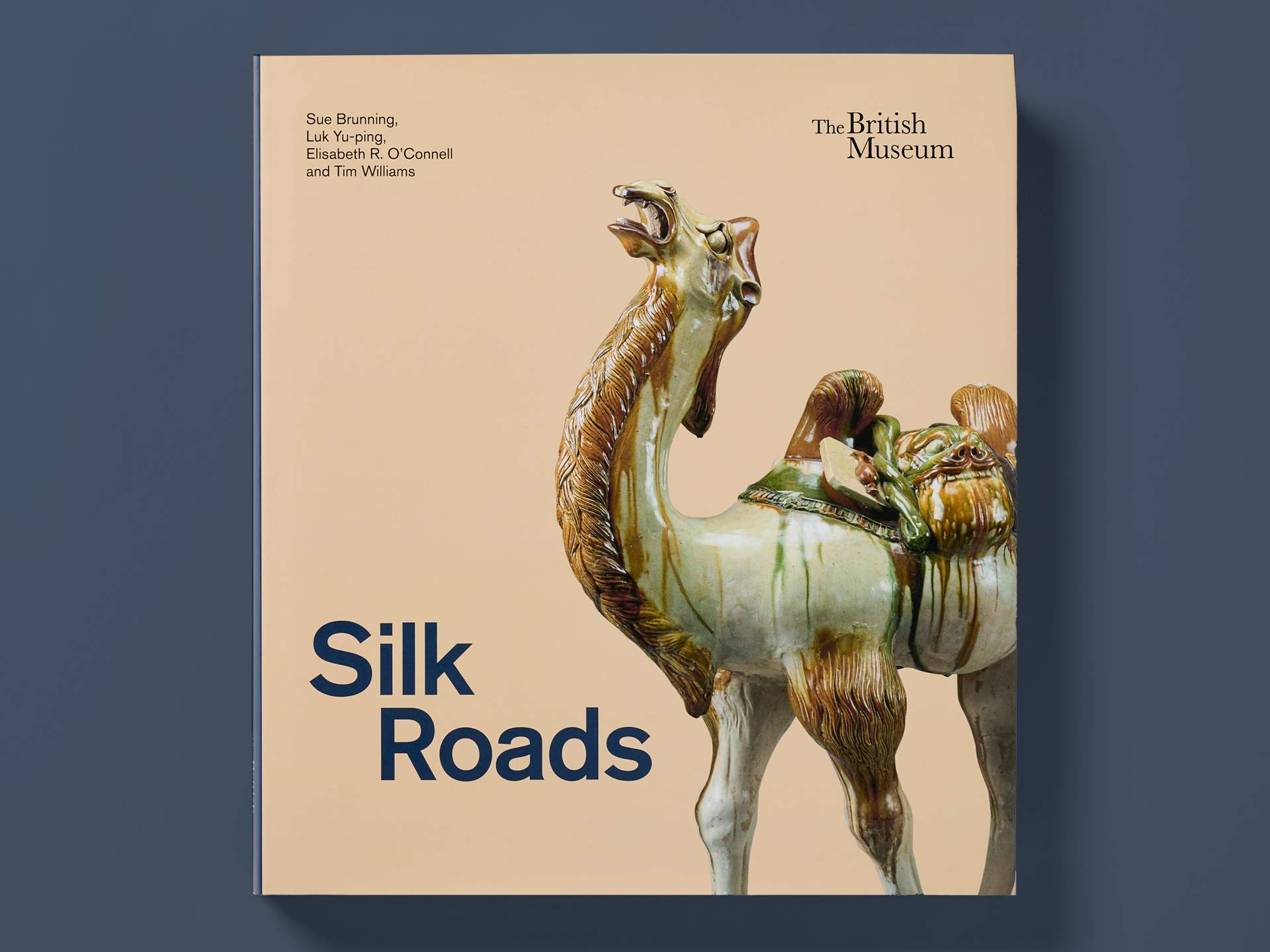 Book titled "Silk Roads" on a dark blue background, featuring a glazed ceramic camel sculpture photographed against a warm beige backdrop. The British Museum logo appears at the top right, with authors Sue Brunning, Luk Yu-ping, Elisabeth R. O’Connell, and Tim Williams listed at the top left.
