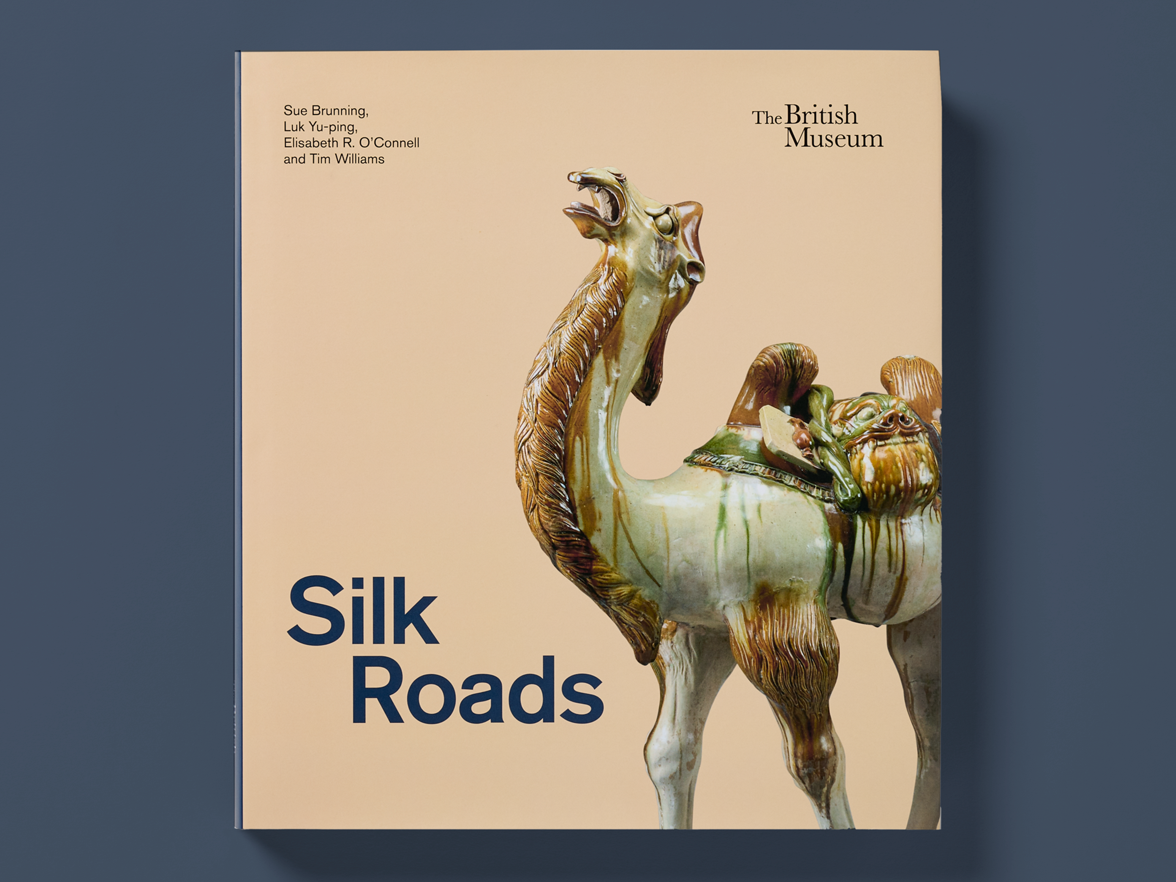 Book titled "Silk Roads" on a dark blue background, featuring a glazed ceramic camel sculpture photographed against a warm beige backdrop. The British Museum logo appears at the top right, with authors Sue Brunning, Luk Yu-ping, Elisabeth R. O’Connell, and Tim Williams listed at the top left.