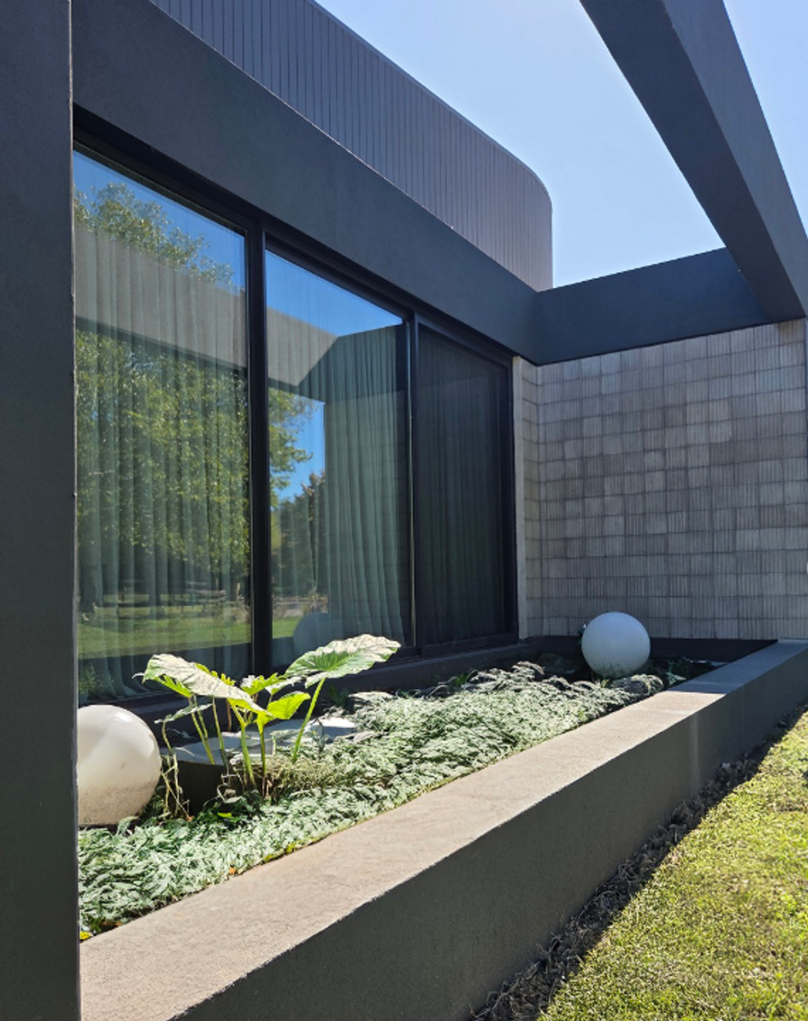 Fachada de vivienda moderna revestida con baldosa 6 panes gris 20×20 junto a cantero con plantas.
