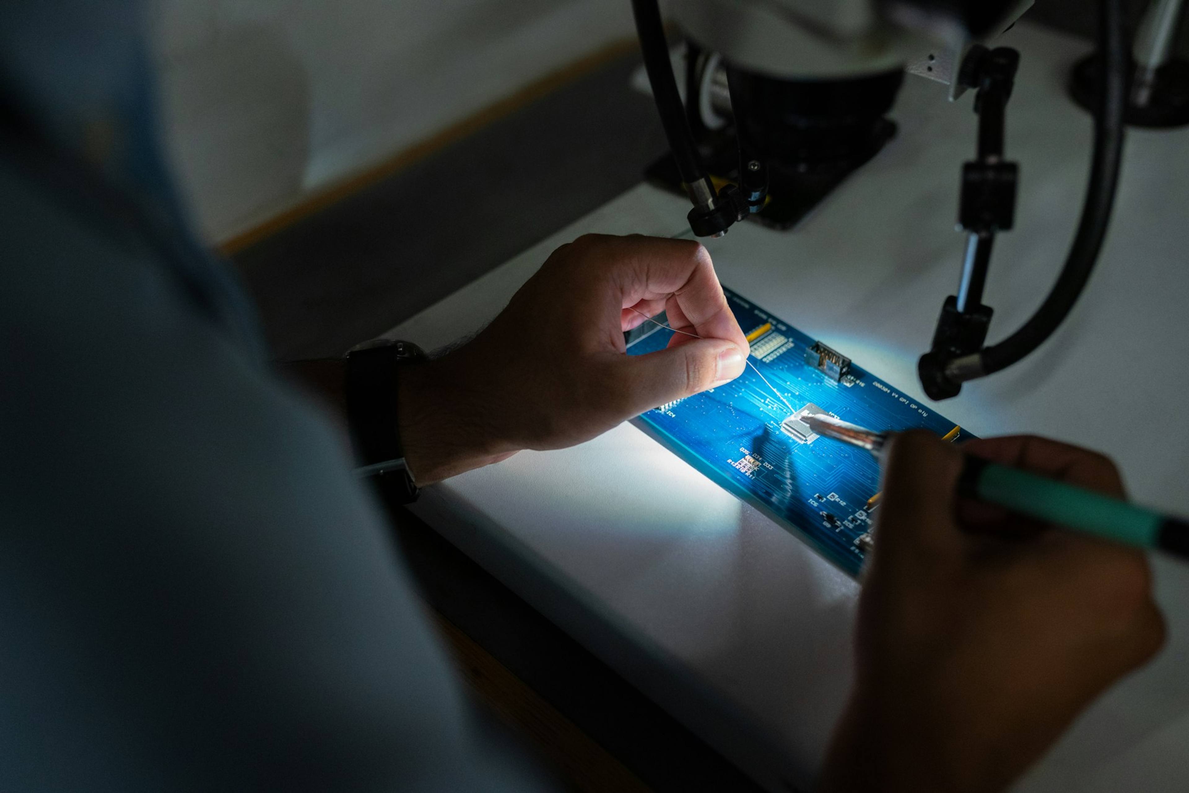 A technician repairing a circuit board under a lamp