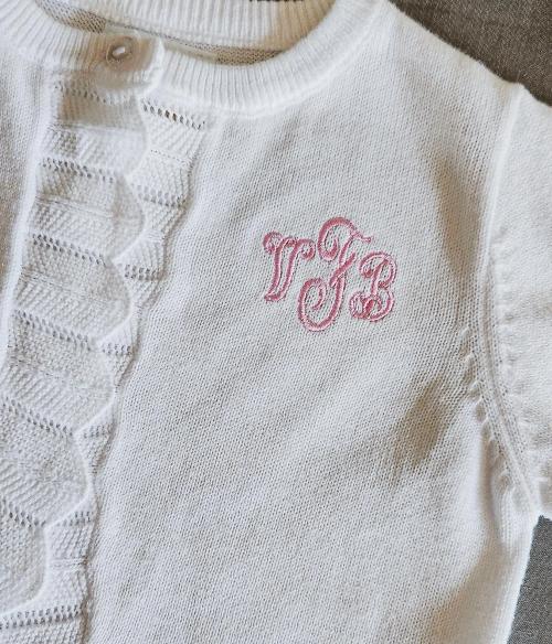 Pink script three-letter monogram embroidered on a white knit sleeveless baby sweater