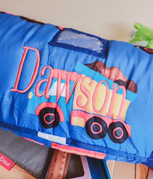 Red script name "Dawson" embroidered over an applique dump truck design on a blue baby blanket