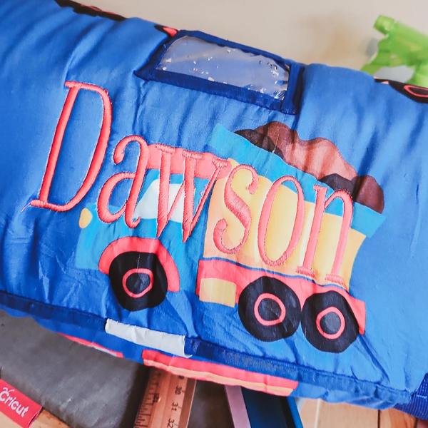 Red script name "Dawson" embroidered over an applique dump truck design on a blue baby blanket