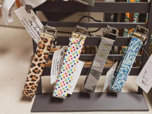 Four fabric wristlet key fobs on a display rack in leopard print, rainbow polka dot, camo, and blue paisley patterns