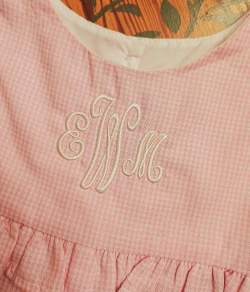 White script three-letter monogram "EJM" embroidered on the bodice of a pink gingham baby dress