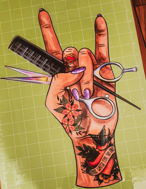 Heat transfer vinyl design of a tattooed hand making a rock-on gesture while holding hairstylist scissors and a comb, on a cutting mat