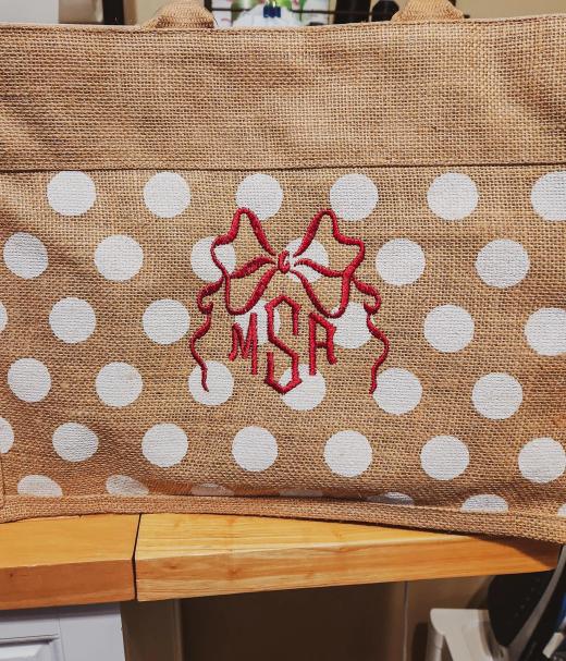 Three-letter red script monogram with bow and star ribbon design on a burlap tote bag with white polka dots