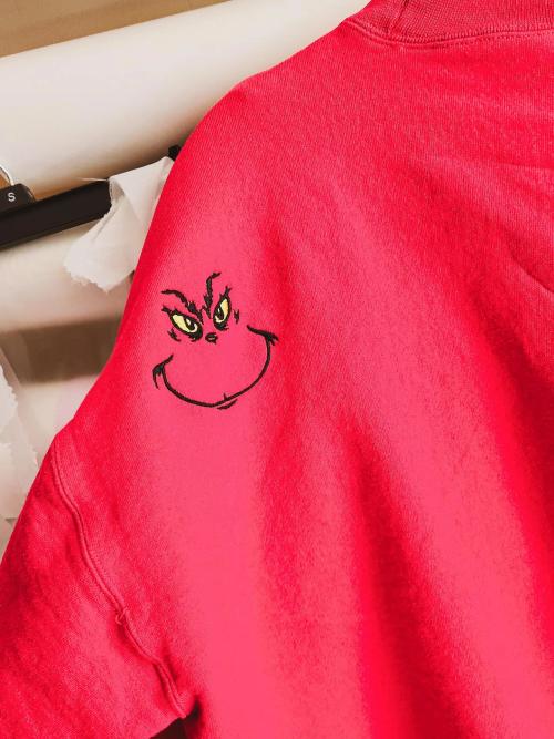 Grinch face embroidered on the shoulder of a red sweatshirt