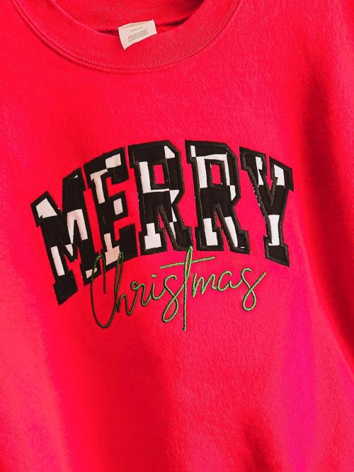 "Merry Christmas" appliqued in black-and-white checkered patch letters with green cursive script on a red sweatshirt