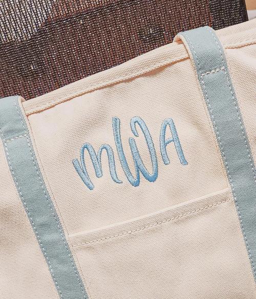 Light blue script three-letter monogram "MWA" on a cream canvas tote bag with matching light blue straps