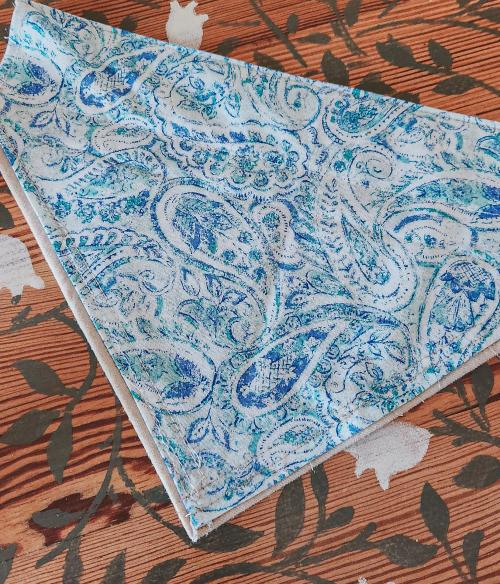 Folded blue and white paisley-print pet bandana laid on a wood floor