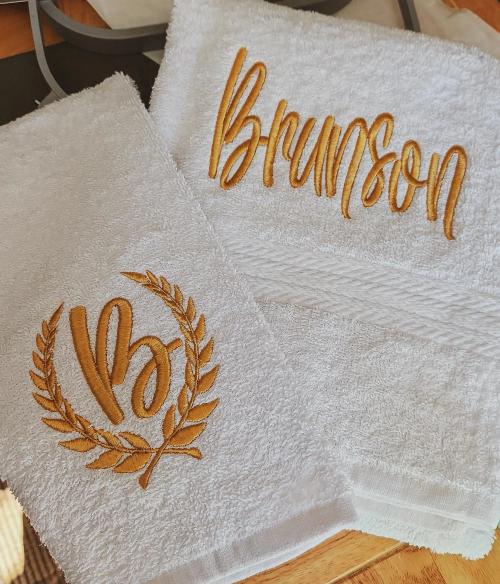 White terrycloth hand towels embroidered with a gold script name "Brunson" and a matching gold laurel wreath letter "B" monogram