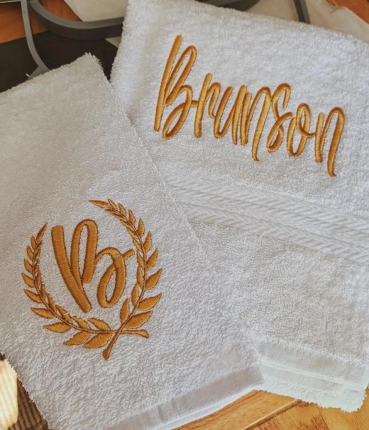 White terrycloth hand towels embroidered with a gold script name "Brunson" and a matching gold laurel wreath letter "B" monogram