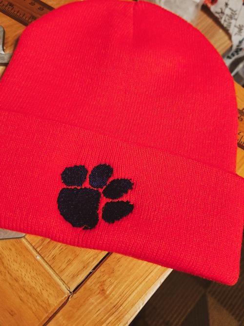 Red knit beanie cap with a navy paw print embroidered on the folded cuff