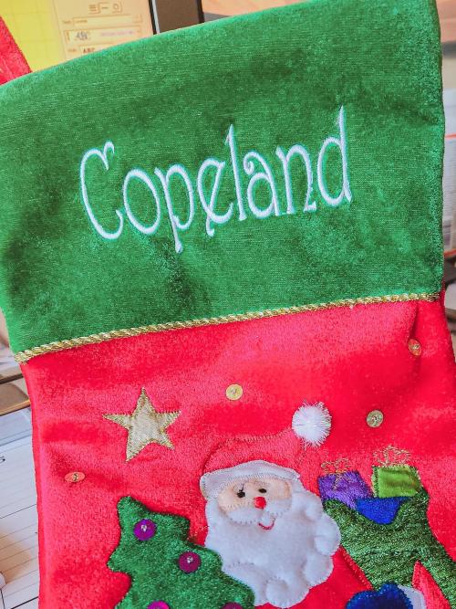 White script name "Copeland" embroidered on the green velvet cuff of a red Christmas stocking with a Santa applique
