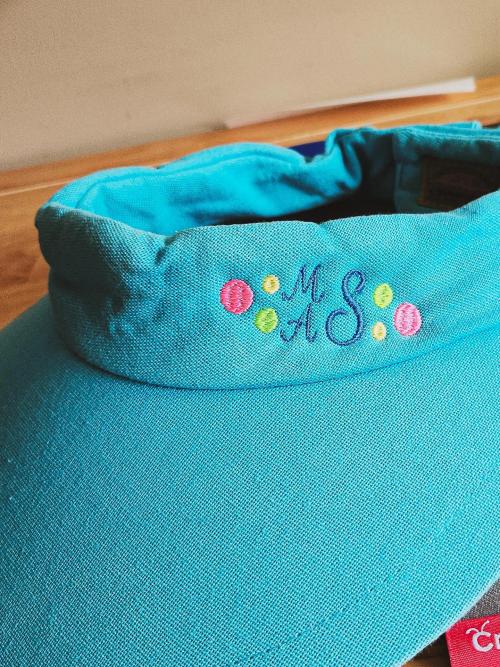 Turquoise wide-brim sun hat embroidered with a navy "MAS" monogram surrounded by colorful polka dots