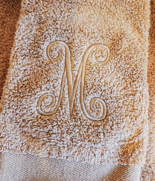 Single pink cursive script letter "S" monogram embroidered on stacked sage green terrycloth towels