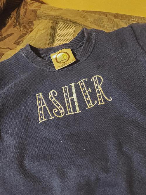 Cream block-letter name "Asher" with dot accents embroidered on a navy toddler crewneck sweatshirt