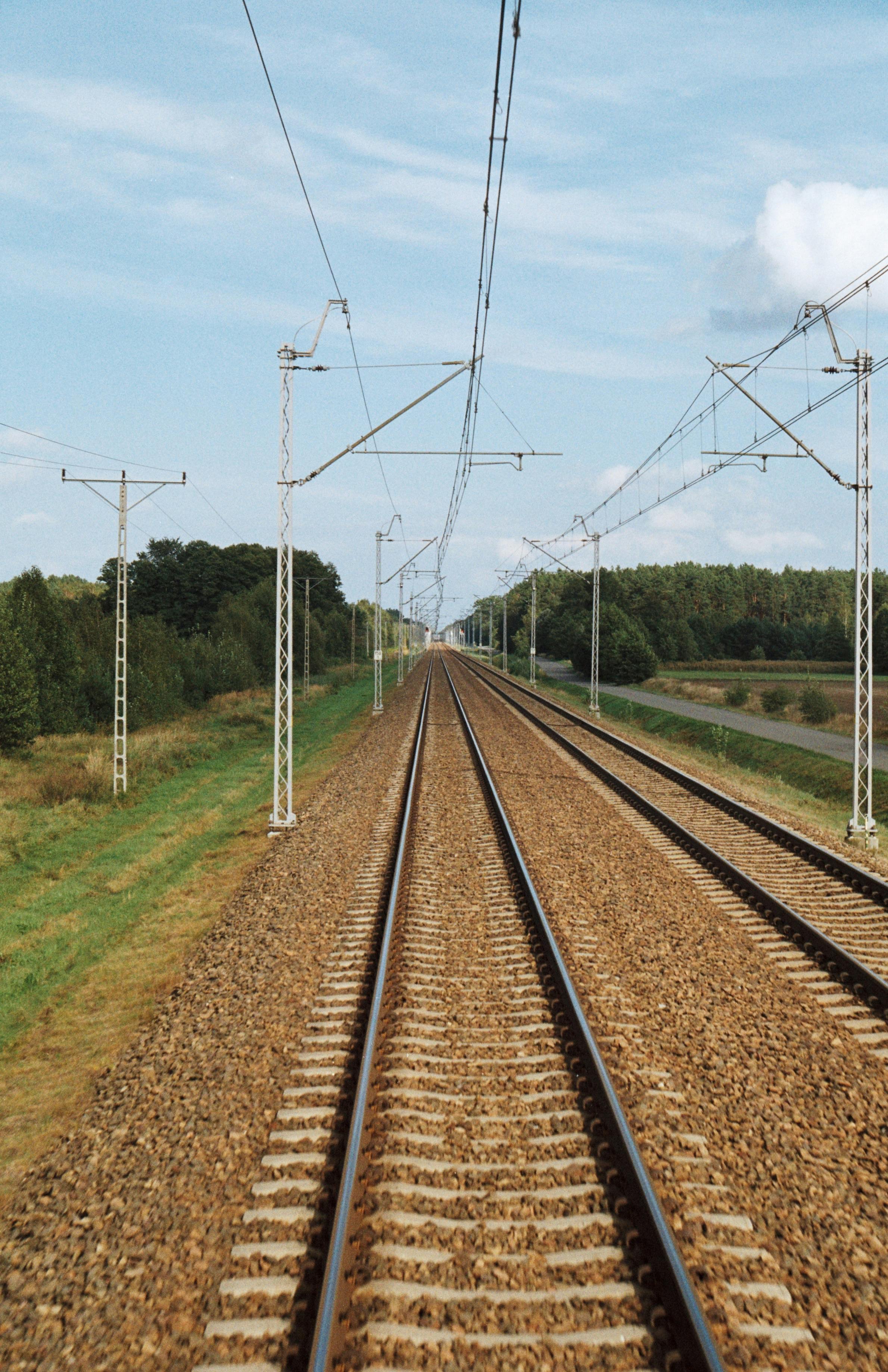 Tuščios geležinkelio vėžės su elektros linijomis kaimo peizaže