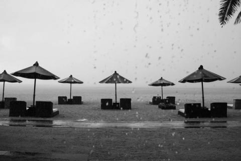 A serene rainy beach with umbrellas, chairs, and raindrops visible.