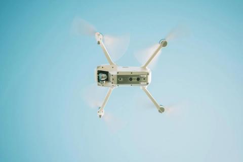 Baltas dronas skrenda mėlyname danguje