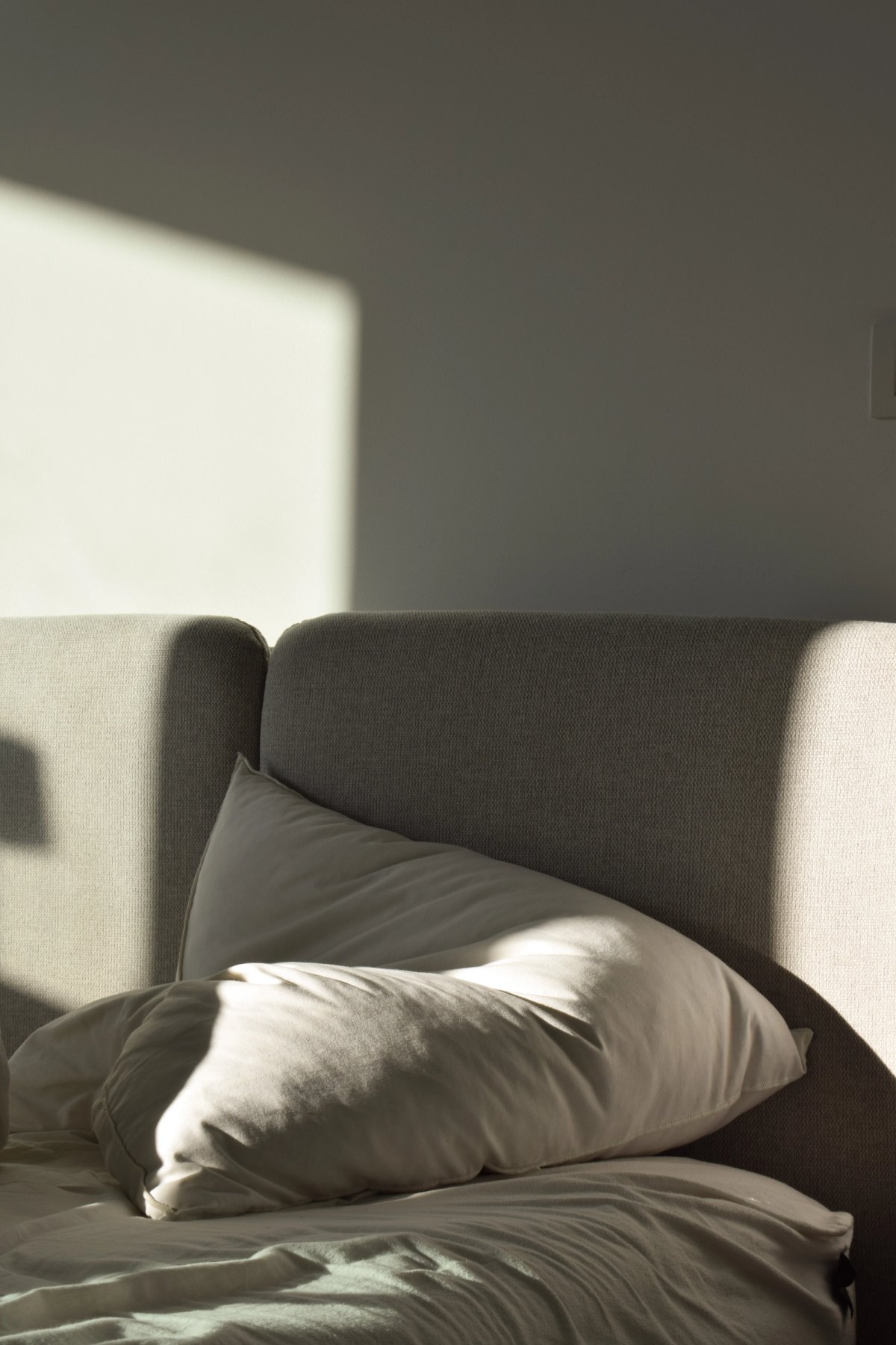 Soft cushions on a linen sofa with late afternoon sunlight falling across the wall behind