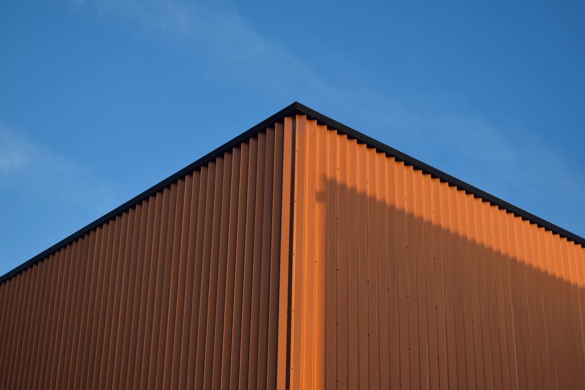 Corner of a rust-orange corrugated metal building against a blue sky at golden hour