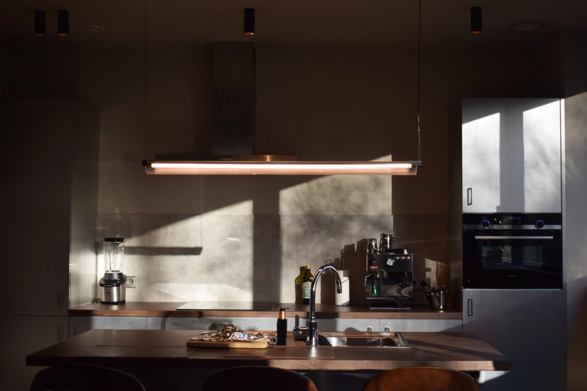 Modern kitchen with walnut worktop and linear pendant light, raking evening sun across the splashback