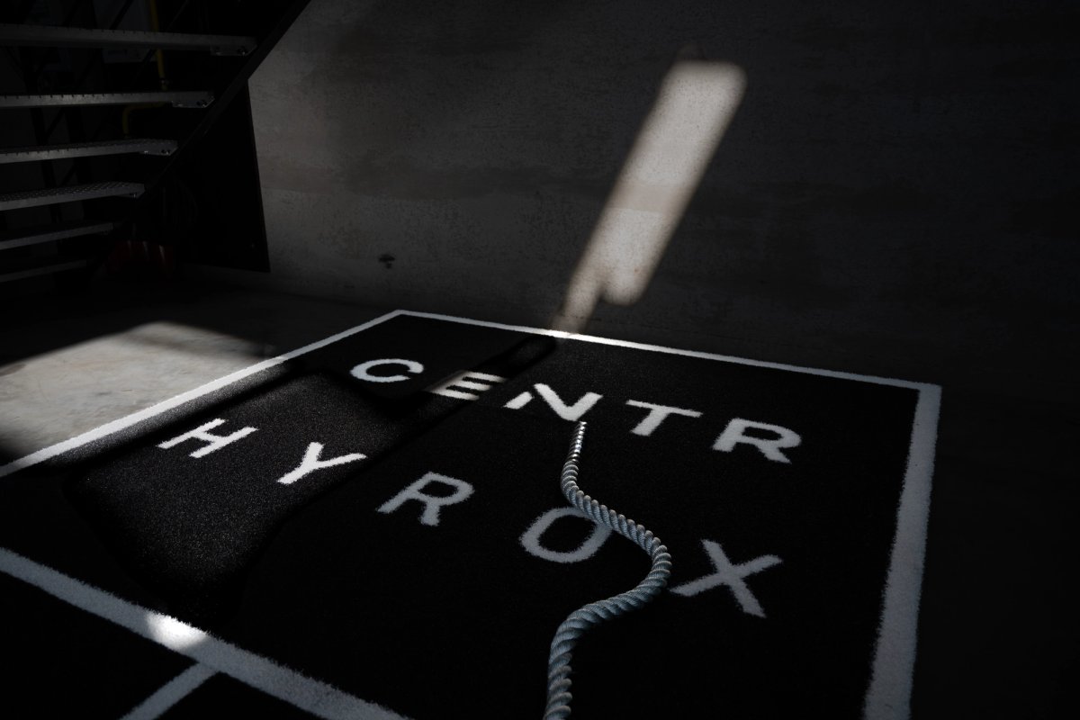 Battle rope on a black Hyrox training mat lit by a shaft of daylight across a concrete floor