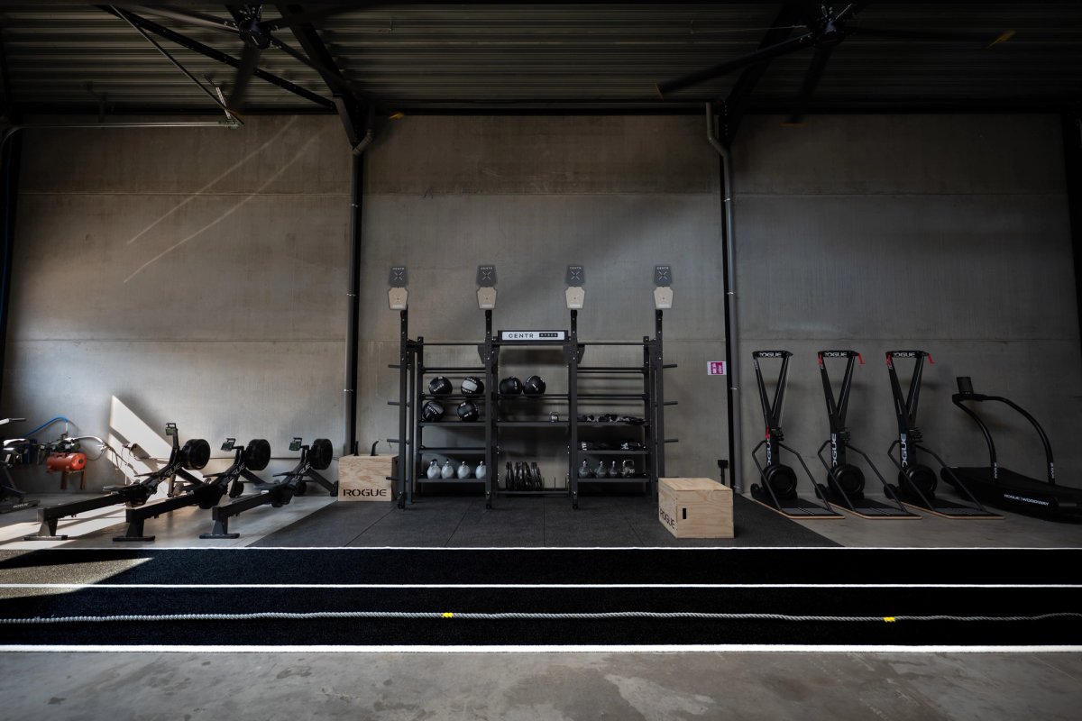 Row of rowing machines, a weights rack and ski ergs along a concrete wall in a gym