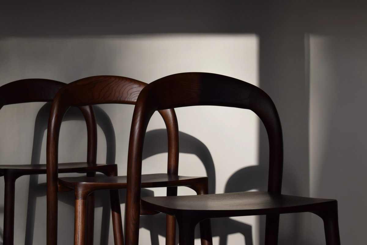 Three curved wooden chairs casting long shadows on a pale sunlit wall