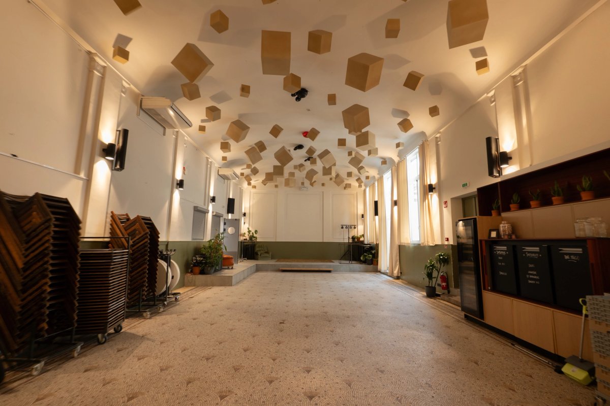 Event hall with a scattered wooden cube ceiling installation, stacked chairs and a bar counter