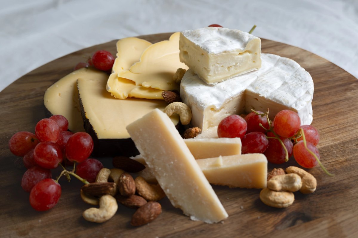 Cheese board with camembert, sliced gouda, aged parmesan, red grapes and nuts on dark wood