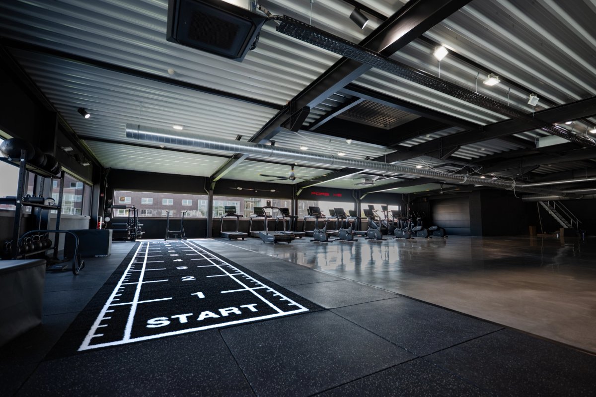 Industrial gym floor with a marked sprint track and a row of treadmills under an exposed steel roof