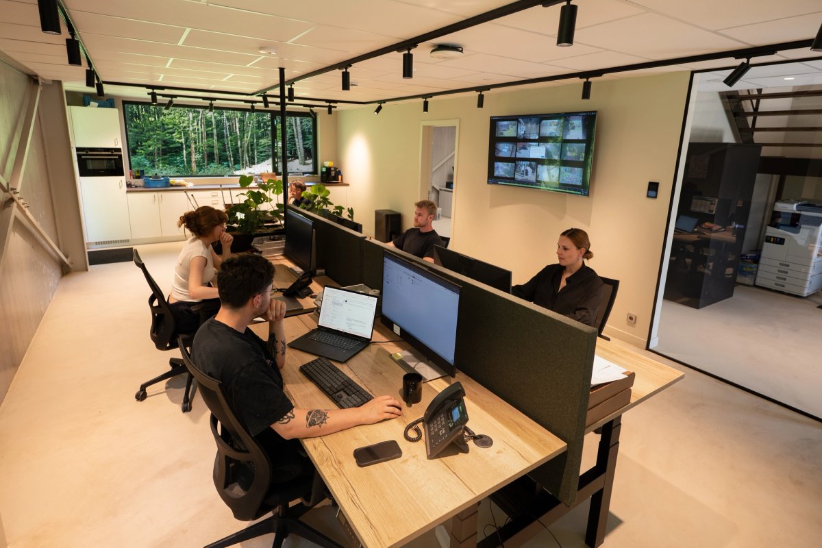 Open-plan office with five colleagues working at a shared desk island under black track lighting