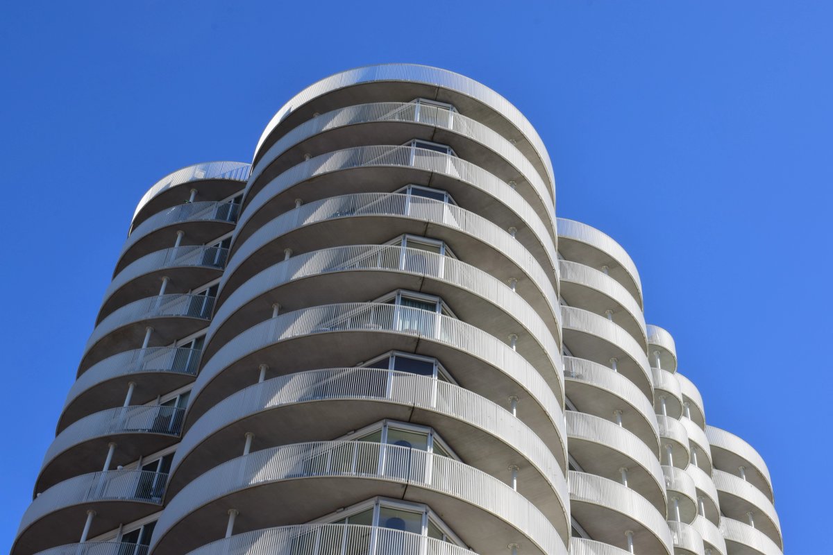 Curved white balconies of an apartment tower stacked against a deep blue sky
