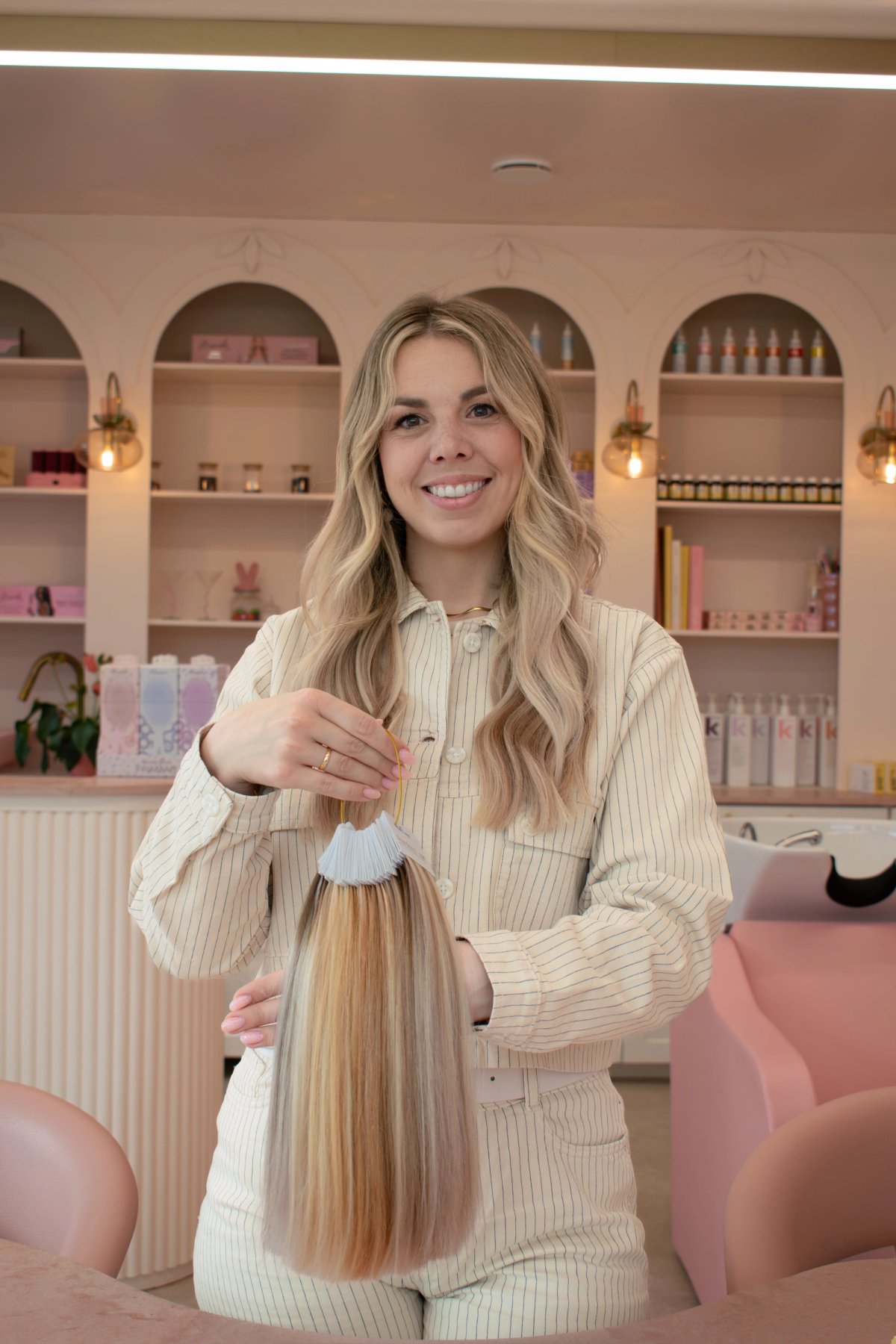 Salon owner holding a fan of hair extension colour samples in a pink and cream salon interior