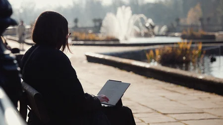 Ellie Stathaki sits on a bench in the park, near the water. She is using her Type Folio keyboard accessory to write on her reMarkable Paper Pro.