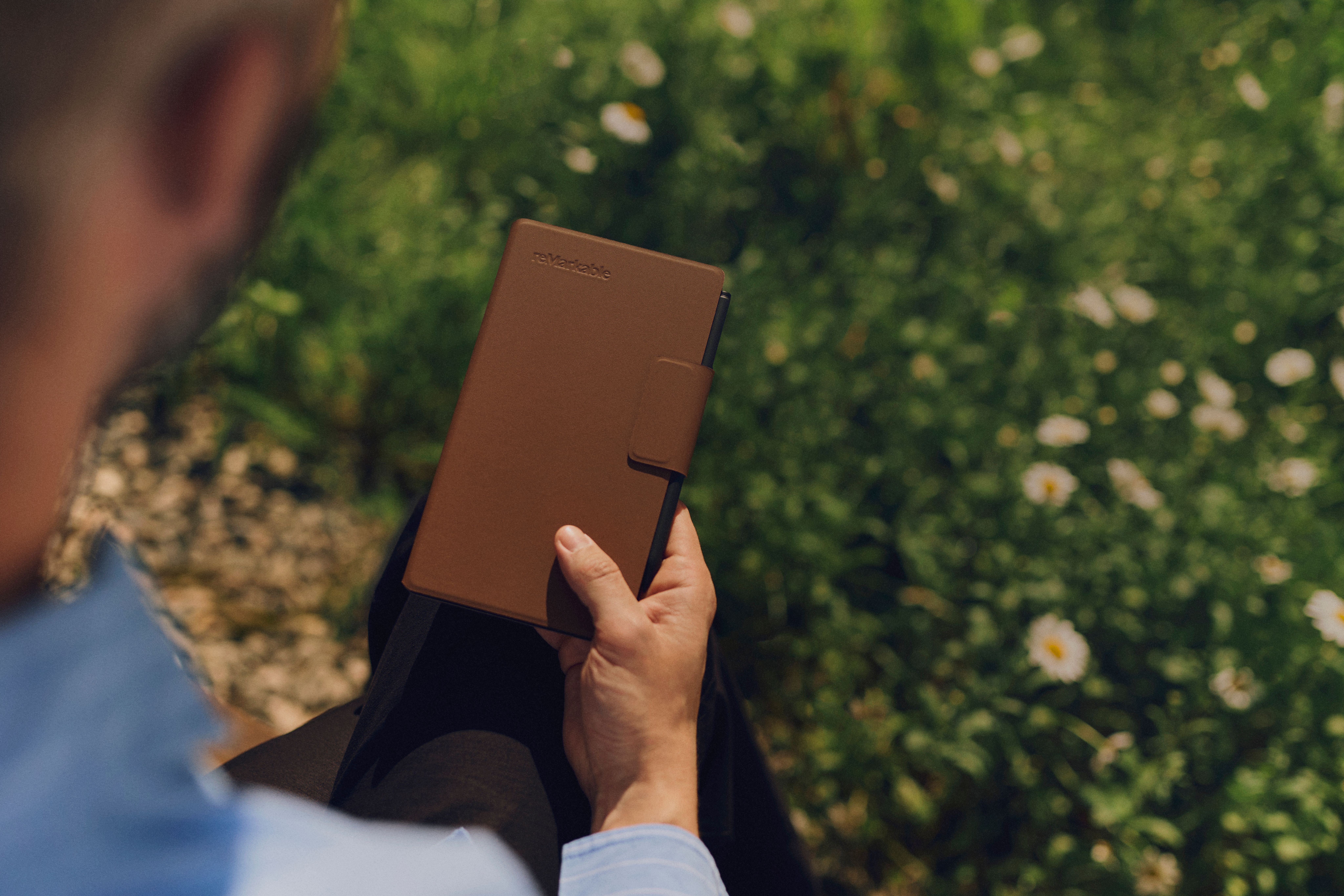 Man holds a reMarkable Paper Pro Move tablet with a brown Book Folio cover outdoors.
