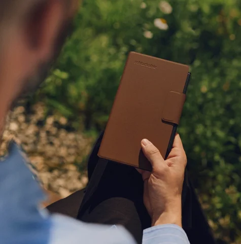 Man holds a reMarkable Paper Pro Move tablet with a brown Book Folio cover outdoors.