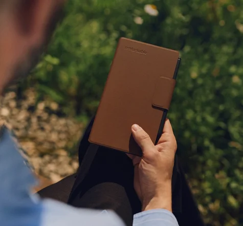 Man holds a reMarkable Paper Pro Move tablet with a brown Book Folio cover outdoors.