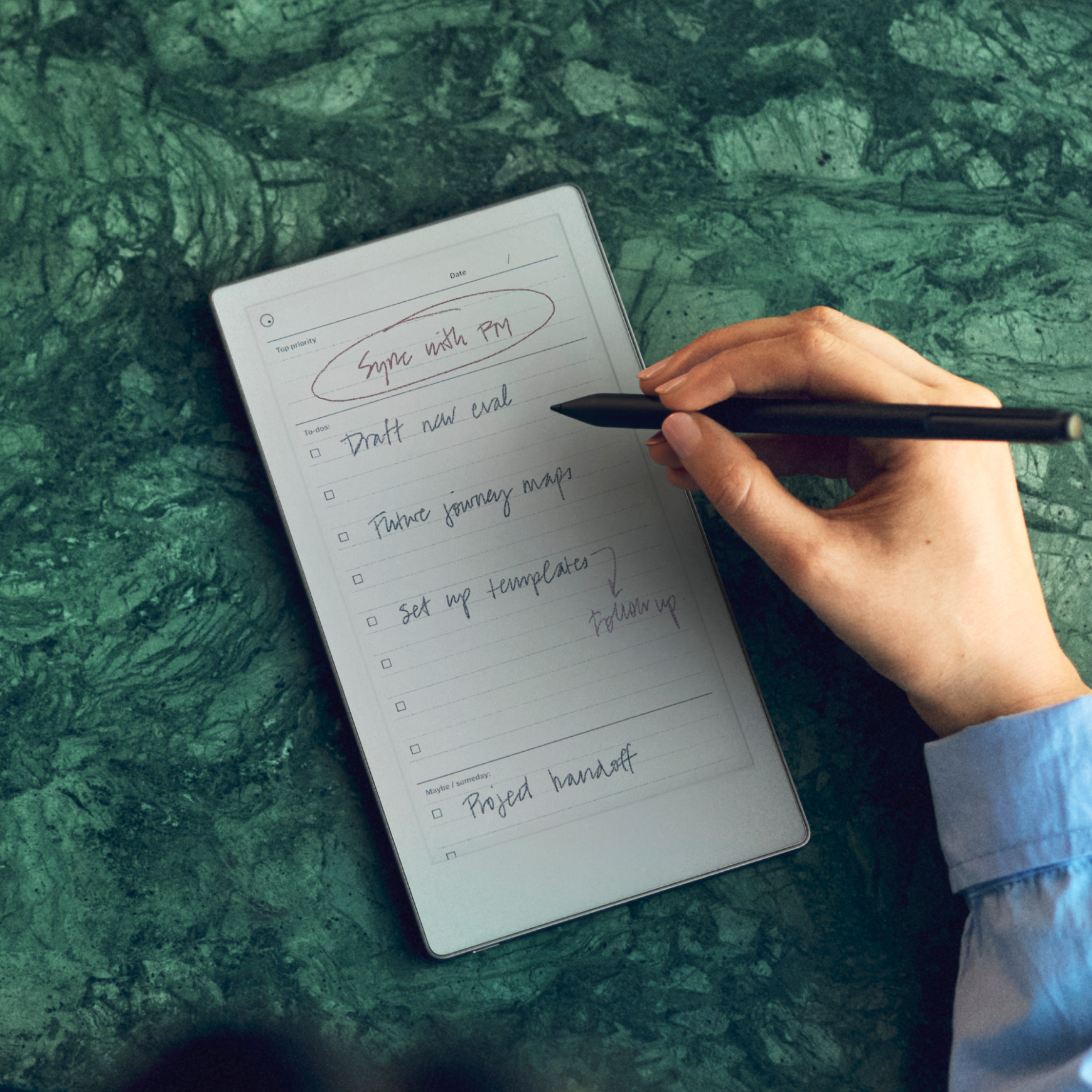 A person writing notes with the Marker Plus on a reMarkable Paper Pro Move resting on a green marble surface.
