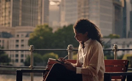 A person using a reMarkable paper tablet while sitting on an outdoor bench writing with the Marker.