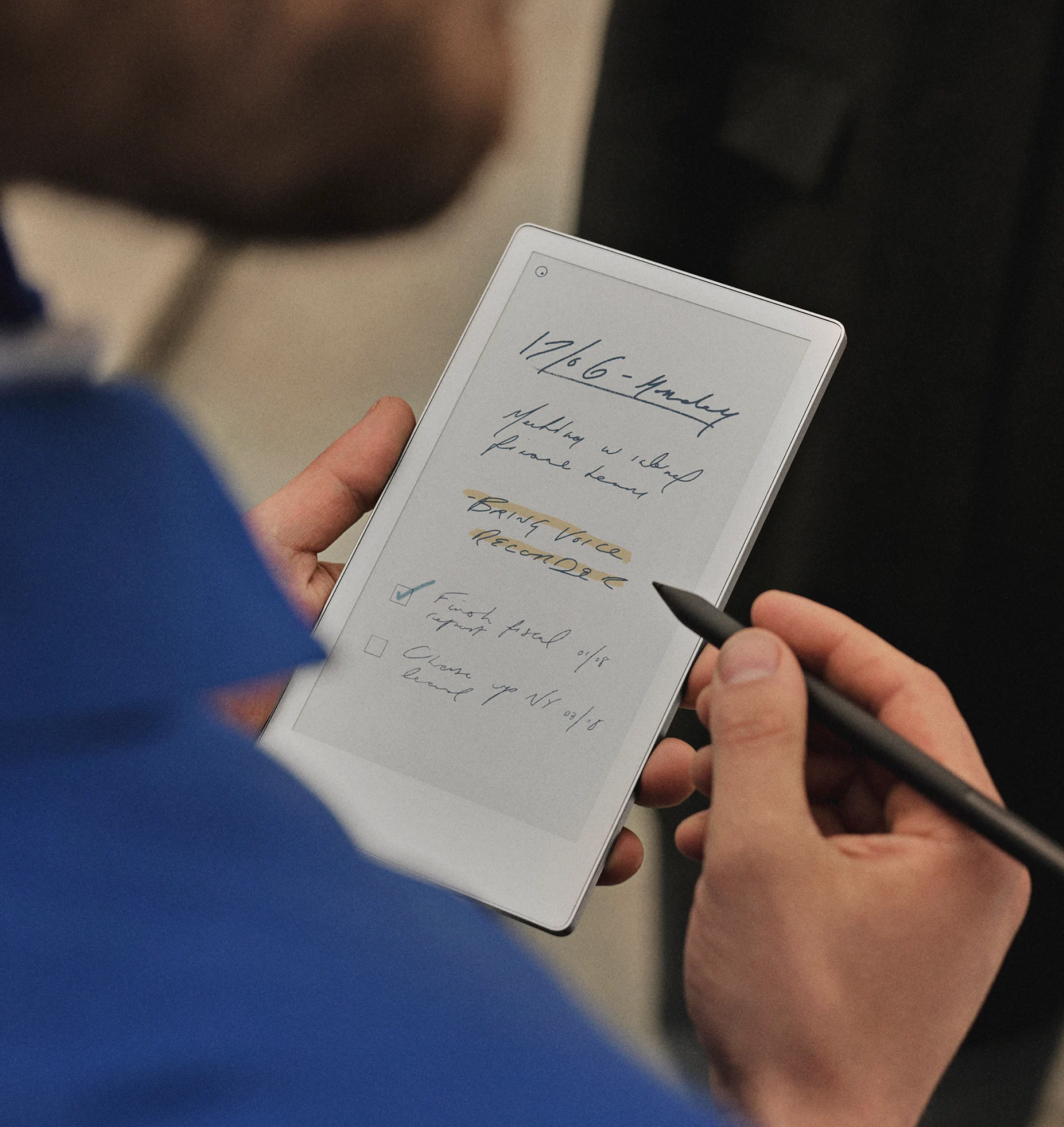 Over-the-shoulder view of a man in a blue jacket standing and writing notes on a reMarkable Paper Pro Move with a Marker Plus, showcasing the device's portability.