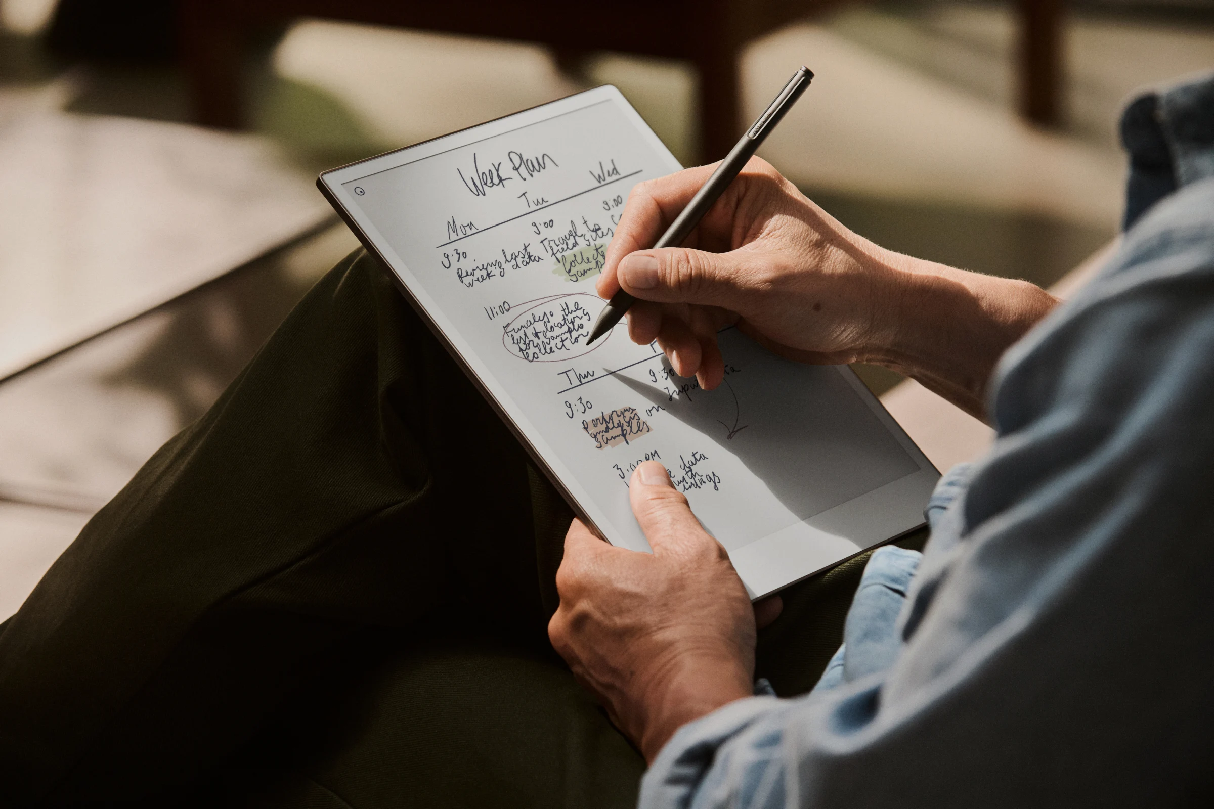 Close-up of a person holding an reMarkable paper tablet and writing weekly schedule notes using a Marker Plus.
