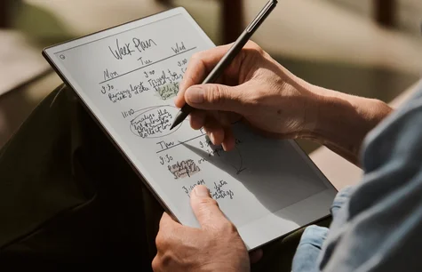 Close-up of a person holding an reMarkable paper tablet and writing weekly schedule notes using a Marker Plus.