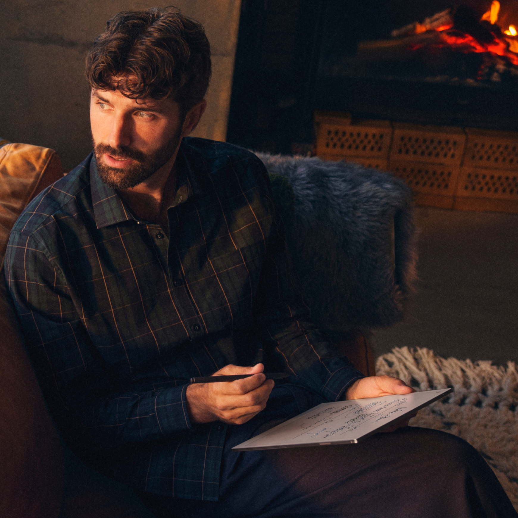 A man in deep focus, writing on a reMarkable Paper Pro in a cozy room.
