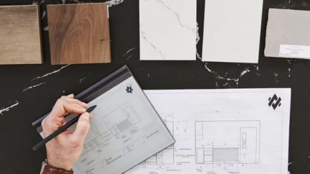 A reMarkable paper tablet displaying architectural plans, with the Marker in a hand resting on the device.